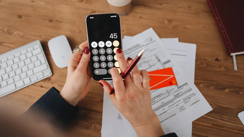 Person calculating salary sacrifice headroom on phone with superannuation paperwork on desk