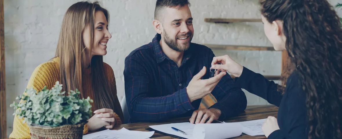 Young Australian couple reviewing paperwork at kitchen table with house keys and laptop showing home loan calculator