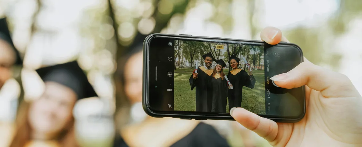 Young Australian woman graduate checking phone showing myGov HECS balance with university campus visible in background
